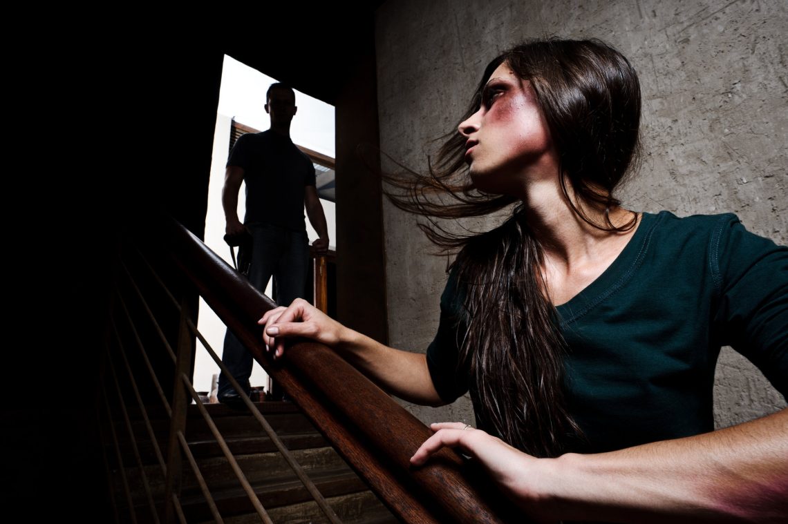 Concept of domestic abuse. Battered woman escaping from man silhouetted at the top of the stairs, in fear of more violence